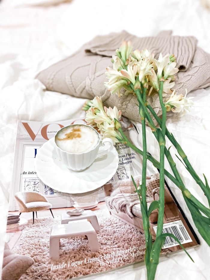 Enjoy a relaxing moment with a latte, soft blanket, and fresh flowers atop Vogue magazine.