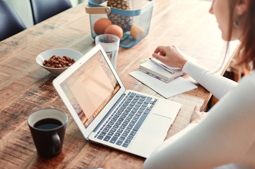 Woman working at home with a laptop, coffee, and healthy snacks on a wooden table.