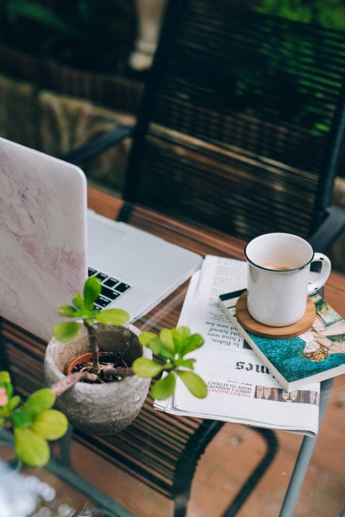 Relaxed workspace setup with a coffee cup, laptop, and plants on a patio table.