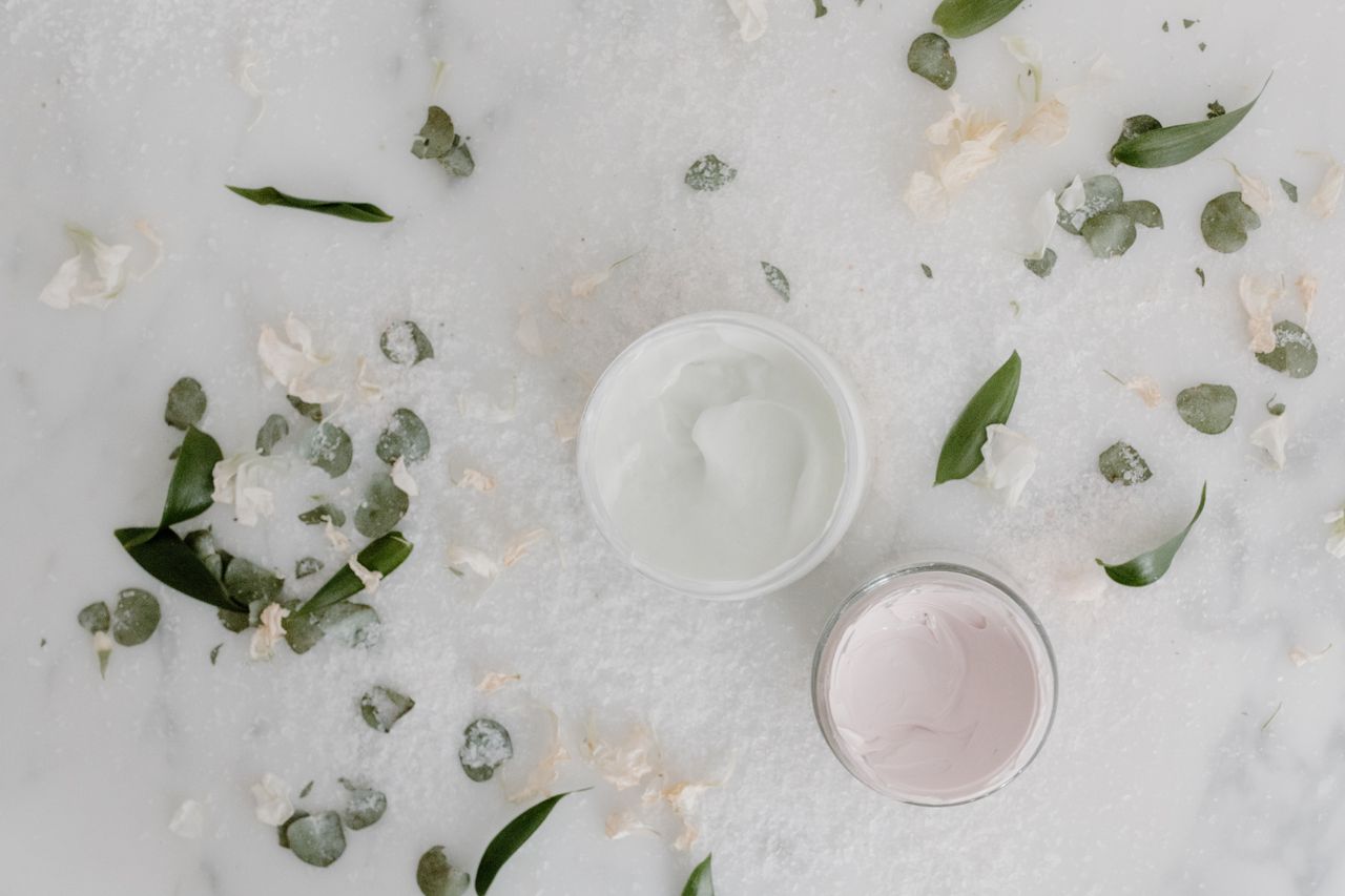 product-04 Flat lay of cosmetic cream jars surrounded by natural leaves and petals, perfect for beauty product promotions.
